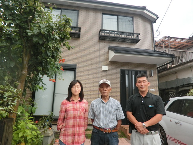 雨漏り修理が完了し笑顔で並ぶ30代女性と70代のお父様、雨漏り診断士の米田。丁寧な説明と点検口設置による屋根裏の確認で、長年の不安が解消した際の記念写真。